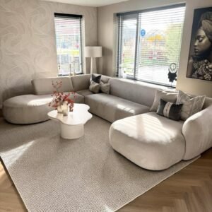 Beige curved modular sectional sofa with deep lounge seating in a bright modern living room.