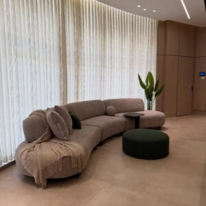 Curved taupe bouclé sectional sofa with rounded ends styled in a modern lounge with sheer curtains and an ottoman