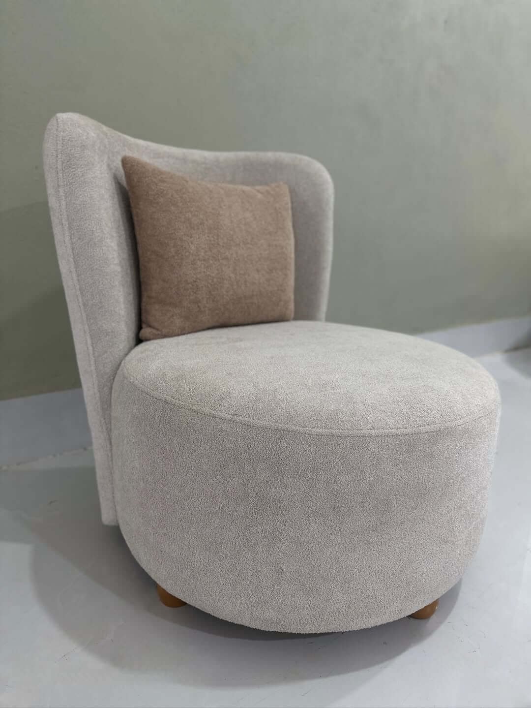Cream accent chair with rounded seat, curved backrest and wood-tone legs for Kenya interiors