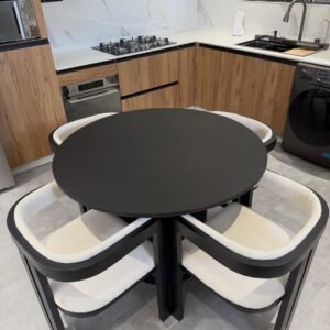 Cream upholstered dining chair with a curved wraparound back and black frame beside a round black dining table.