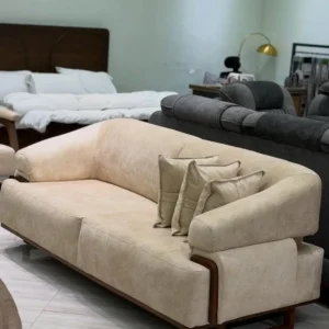 Beige 3 seater sofa with rounded arms, dark wooden trim and three matching scatter cushions in a furniture showroom