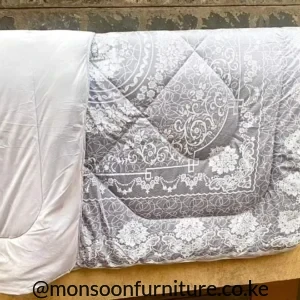 Folded grey and white duvet with ornate floral and scroll patterns and a plain white section visible.