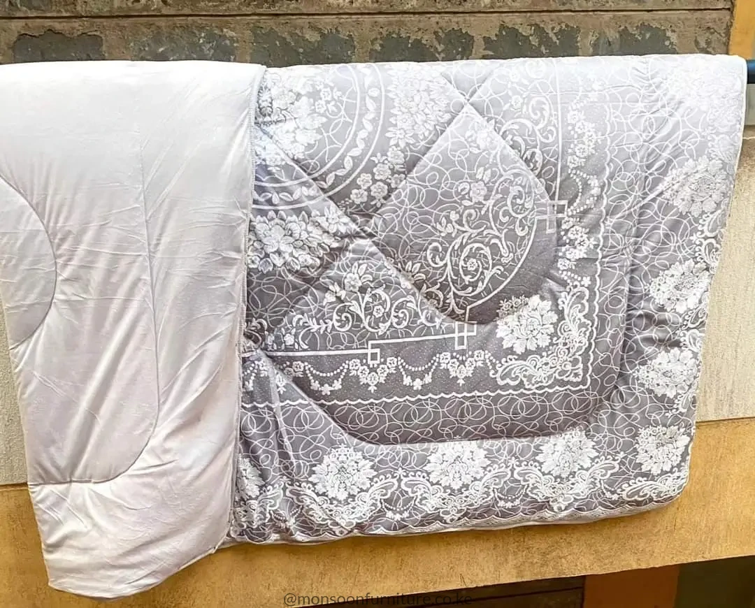 Folded grey and white duvet with ornate floral and scroll patterns and a plain white section visible.