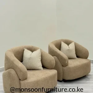 Two beige rounded accent chairs with textured upholstery, dark feet and light cream loose cushions on a pale floor.