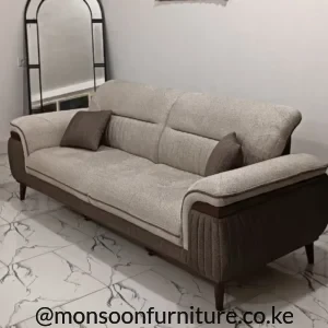 Beige sofa with dark taupe channelled side panels, warm brown arm trim, tapered legs and two dark cushions.