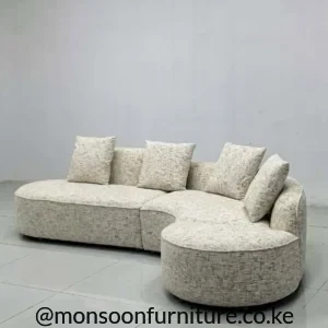 Light beige curved modular sectional sofa with a rounded end seat, low profile and matching neutral cushions.