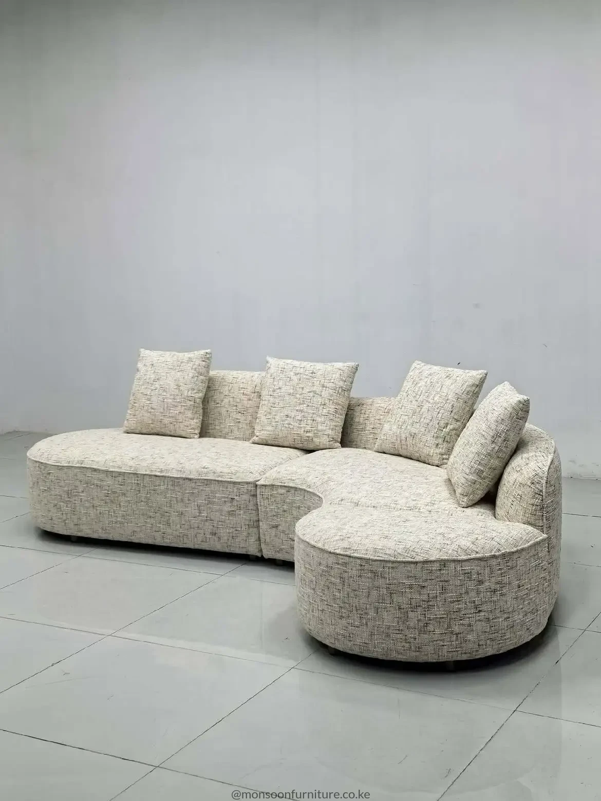 Light beige curved modular sectional sofa with a rounded end seat, low profile and matching neutral cushions.