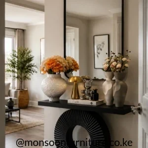 Black slim entryway table with a large ribbed ring-shaped support beneath a tall rounded-corner wall mirror.