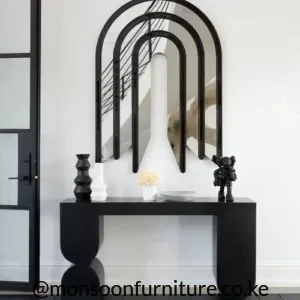 Black sculptural console table with slim top and rounded asymmetric end supports beneath layered arched wall mirrors.
