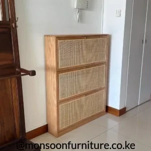 Tall brown shoe cabinet with three stacked light woven front panels and small brass-tone pulls in a hallway.