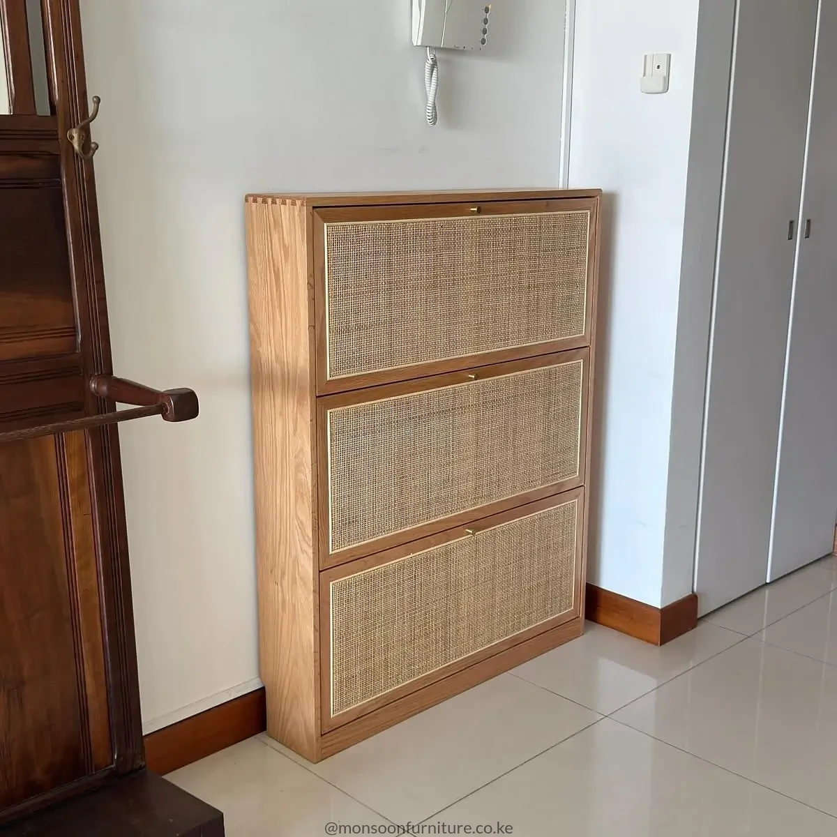 Tall brown shoe cabinet with three stacked light woven front panels and small brass-tone pulls in a hallway.
