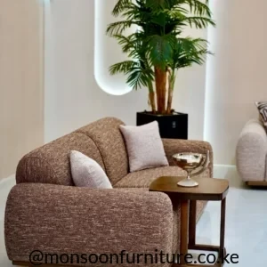 Brown textured sofa with rounded arms, segmented back, light neutral cushions and a slim wood-tone base in a bright living room.
