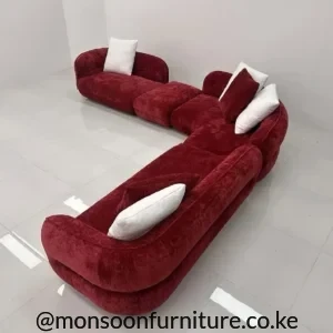 Burgundy curved modular sectional sofa with rounded low back and white contrast cushions in a studio setting.