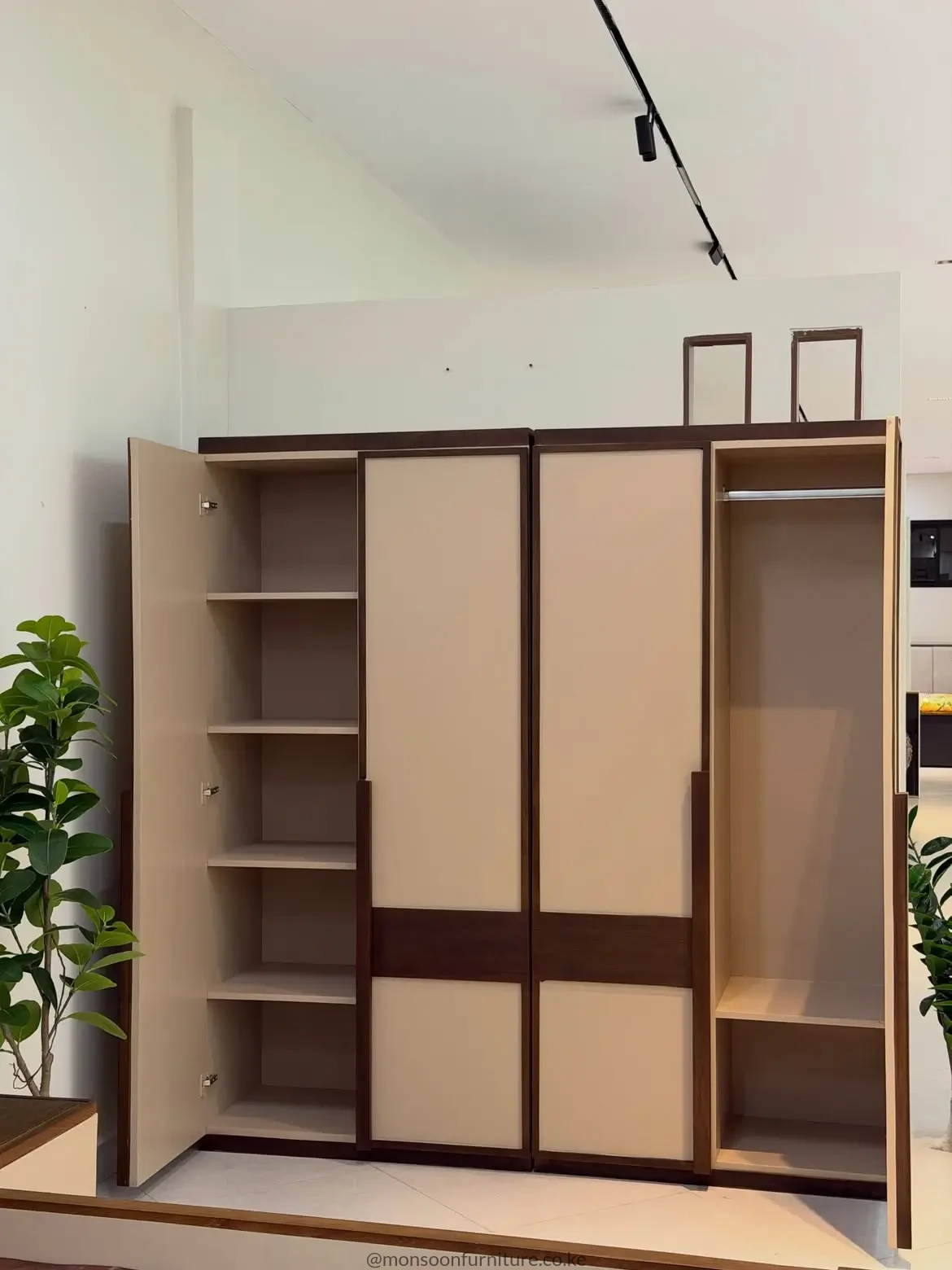 Cream four-door wardrobe with dark wood trim, open shelving and a hanging rail displayed in a furniture showroom.