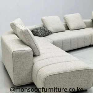 Cream modular sectional sofa with extended chaise, low squared arms, separate padded back cushions and textured upholstery.
