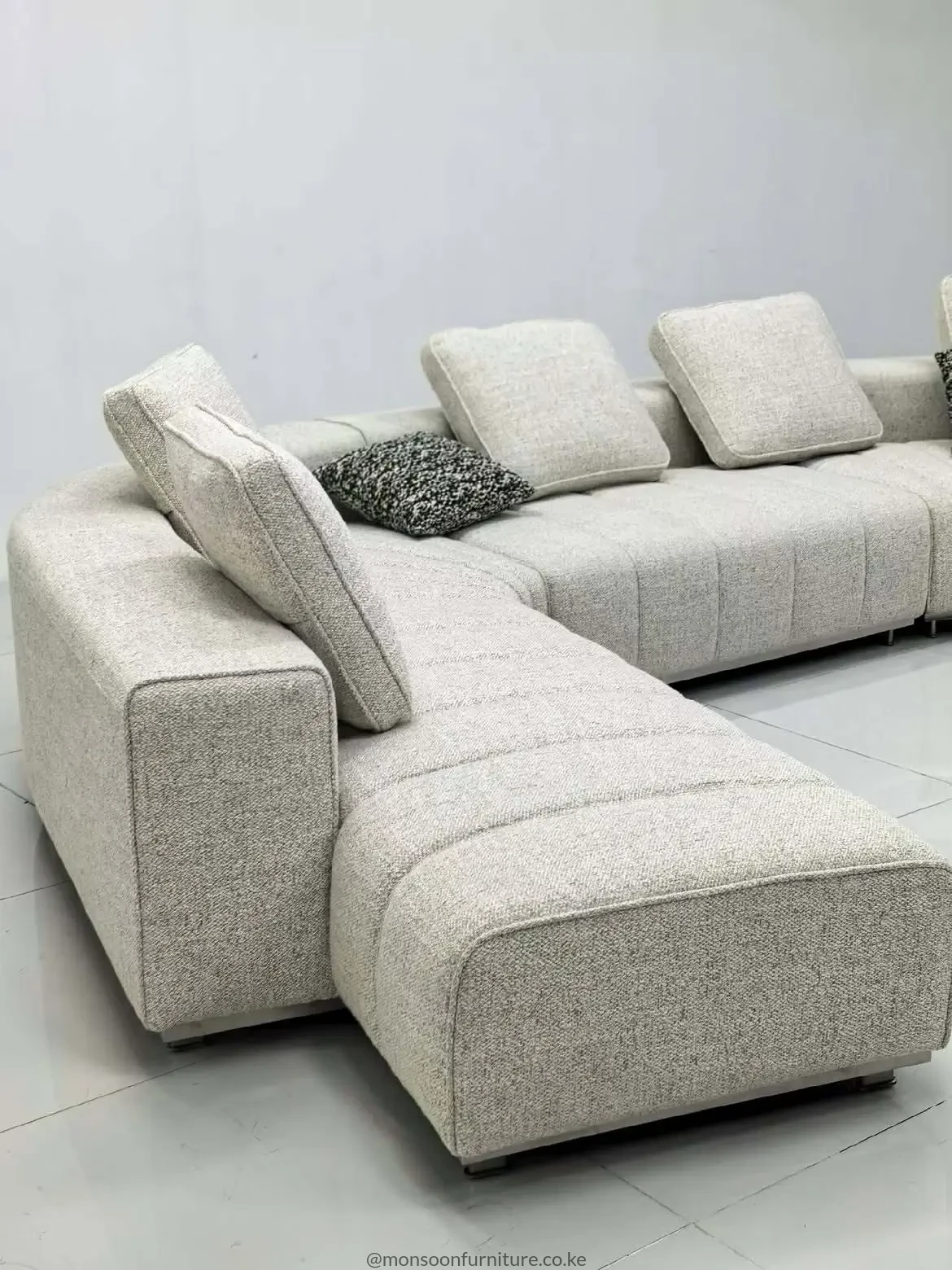 Cream modular sectional sofa with extended chaise, low squared arms, separate padded back cushions and textured upholstery.