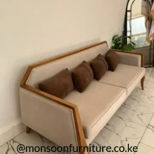Cream sofa with warm brown outline trim, slim angled legs and five brown cushions on a white marble-look tiled floor.
