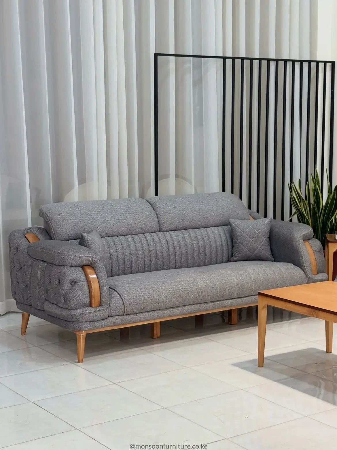 Grey textured sofa with channel-stitched back, button-tufted arms, warm brown accents and raised tapered legs.