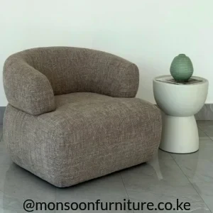 Ivory sculptural side table with a rounded raised-rim top and curved pedestal base beside a taupe upholstered chair.