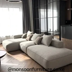 Light beige modular sectional sofa with extended chaise, broad low-profile seats and multiple loose cushions.