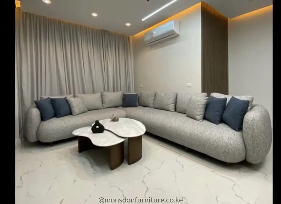 Light grey L-shaped sectional sofa with rounded upholstered arms, grey back cushions and dark blue accent cushions.