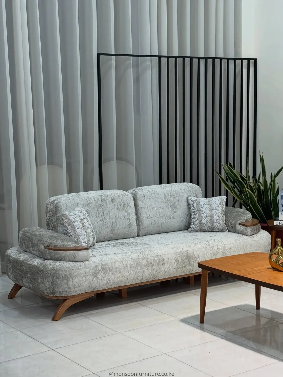 Light grey textured sofa with broad rounded arms, two back cushions, angled brown legs and warm brown arm accents.