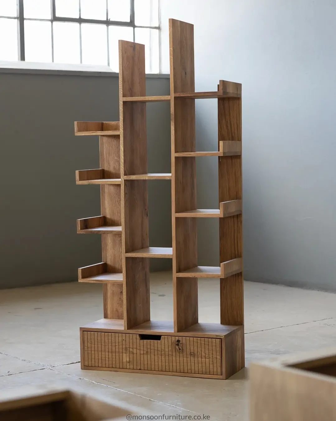 Asymmetrical wood-grain bookshelf with staggered open shelves and one wide drawer at the base