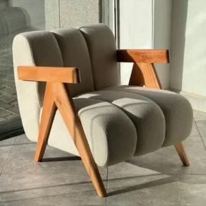 Beige upholstered accent chair with wooden arms and angled legs beside a bright window