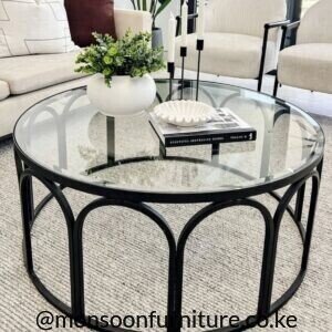 : Round clear glass coffee table with black circular frame and repeated curved arch supports in a neutral living room.