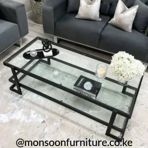 Rectangular black glass coffee table with clear top and lower glass shelf positioned in front of a dark grey sofa.
