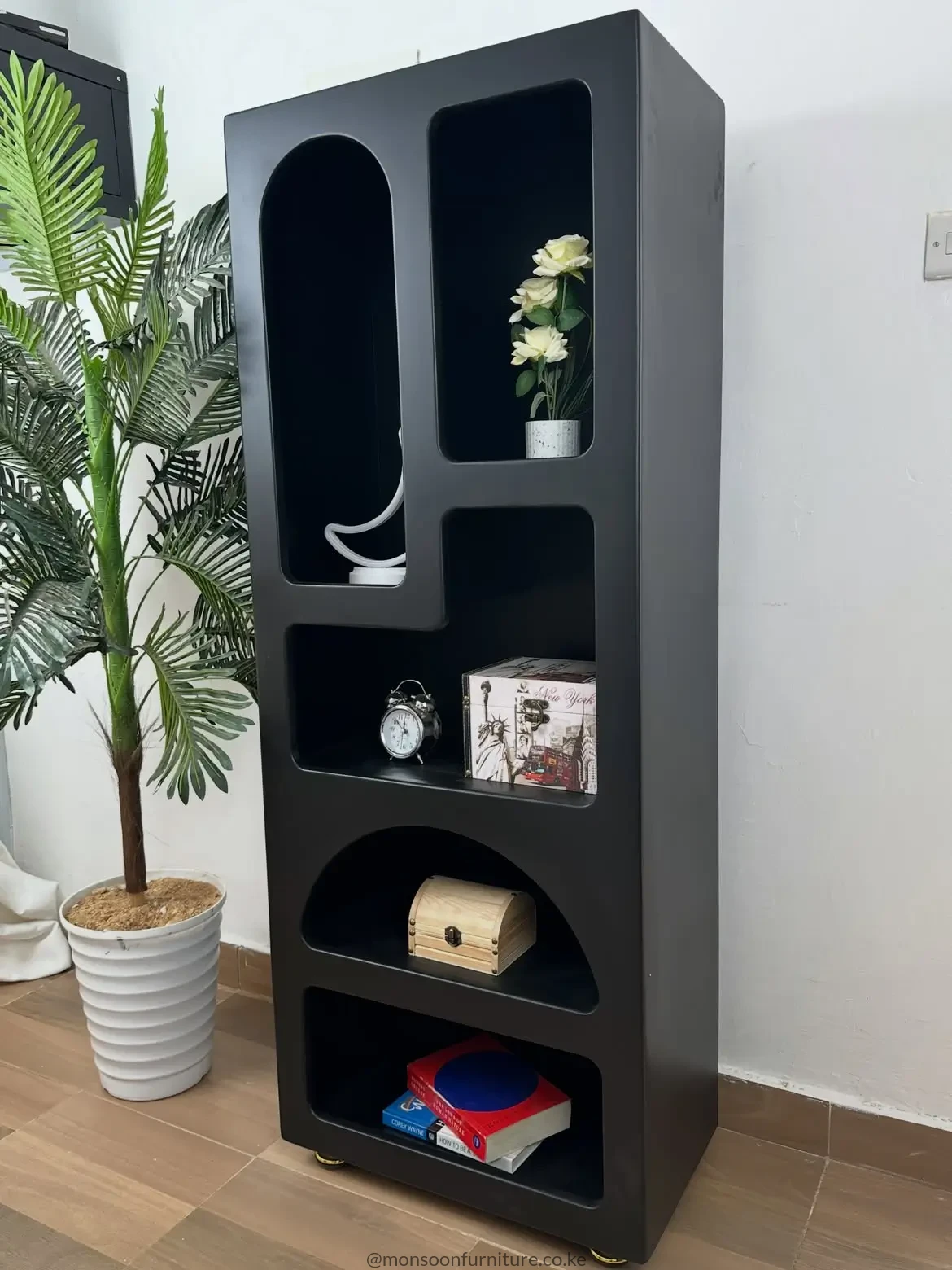 all black bookshelf with five asymmetric open compartments, rounded cut-outs and small gold-tone feet.