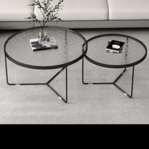 Two round nesting coffee tables with textured clear glass tops and black open frames in front of a light sofa