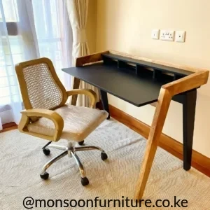 Black home office desk with wood-tone frame, raised rear organizer and cane-back wheeled chair in a bright room.