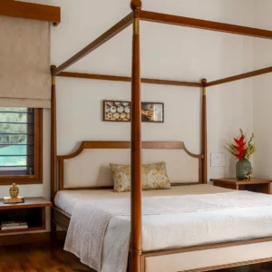 Brown full poster bed with four tall posts, overhead rails and a light upholstered headboard in a bedroom