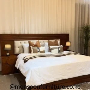 Brown bed frame with wide wood-look panel headboard and light button-tufted centre panel in a styled bedroom