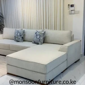 Cream chaise sectional sofa with textured upholstery, slim arms, loose back cushions and low dark wood-tone feet.