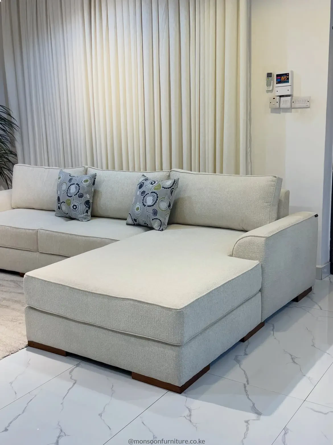 Cream chaise sectional sofa with textured upholstery, slim arms, loose back cushions and low dark wood-tone feet.