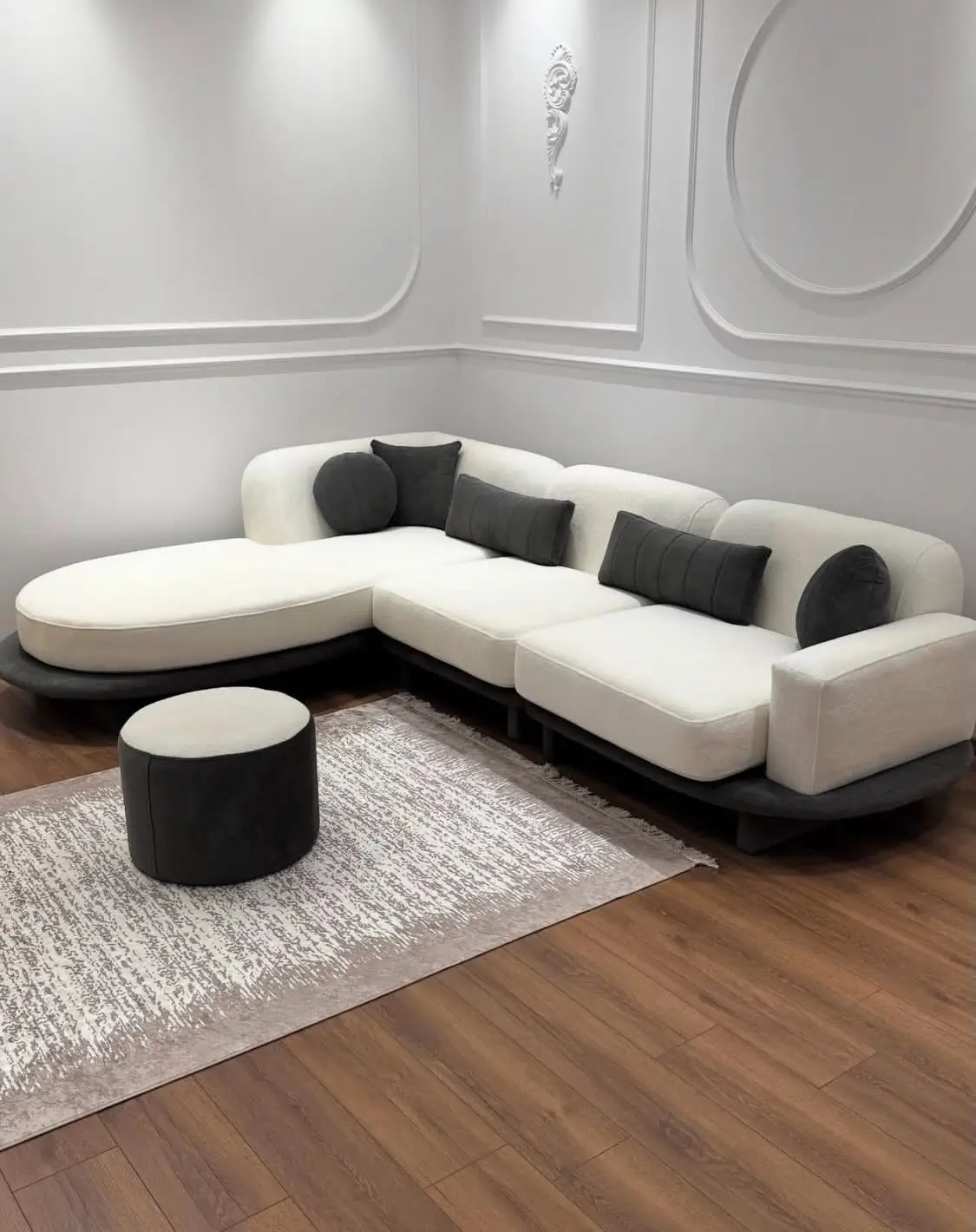Cream curved sectional sofa with rounded chaise, dark base and contrasting dark cushions in a modern living room