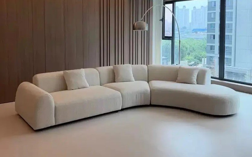 Cream modular sectional sofa with rounded arms, extended chaise and matching cushions in a modern living room