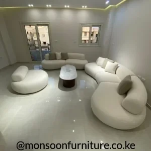 Cream curved upholstered seating with rounded low-profile forms, neutral cushions and a central oval coffee table in a bright living room.