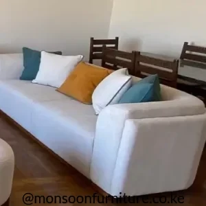 Cream straight upholstered sofa with broad rounded arms and teal, white and mustard accent cushions in a living room