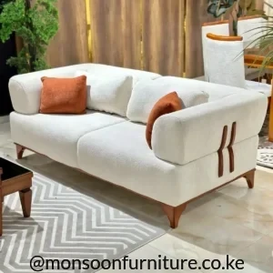 Cream textured two-seater sofa with brown side accents, tapered legs and two rust-orange cushions in a living room.