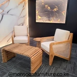 Two cream accent chairs with warm wooden frames and woven side panels beside a slatted table in a dark studio.