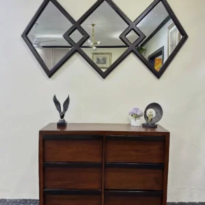 Dark brown six-drawer chest with contrasting dark trim photographed beneath a geometric wall mirror