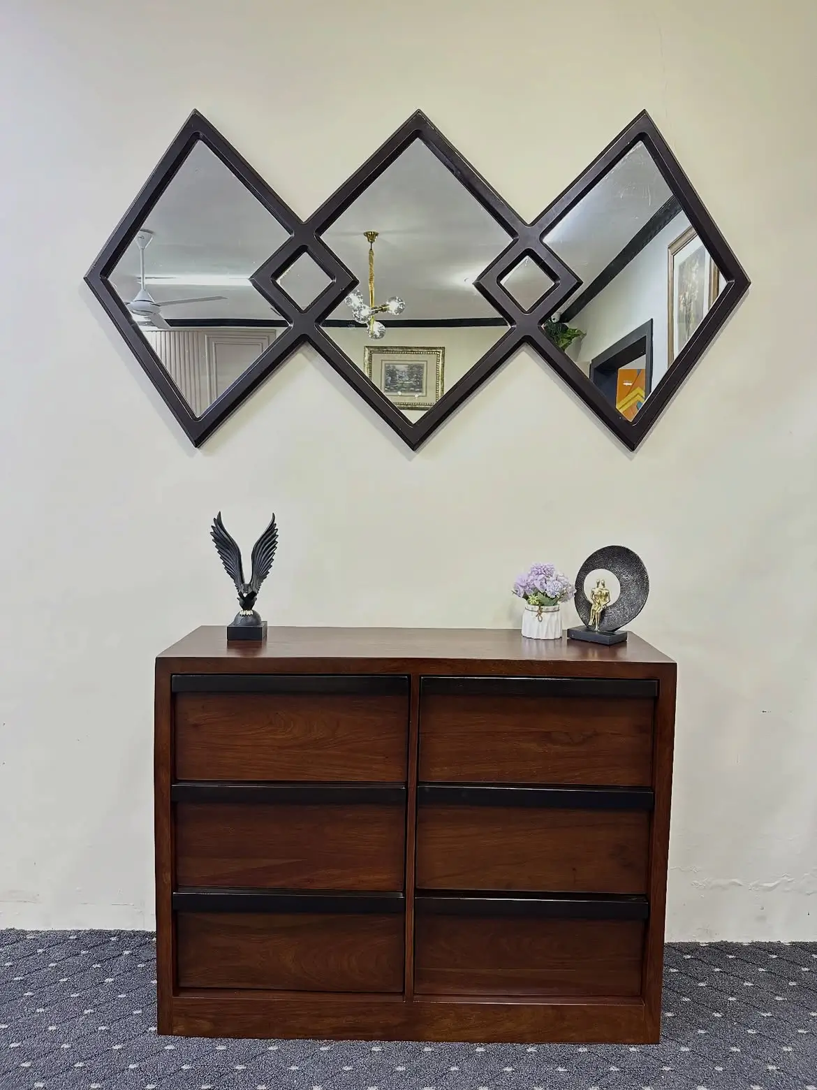 Dark brown six-drawer chest with contrasting dark trim photographed beneath a geometric wall mirror