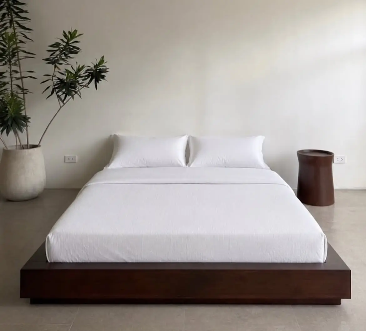 Dark brown low-profile platform bed with white mattress and bedding in a minimalist bedroom