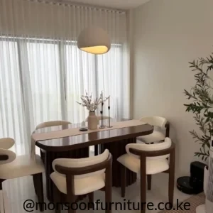 Dark brown rounded dining table with cream upholstered chairs and a fluted central base in a bright dining area