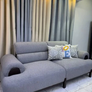 Grey fabric sofa seat with rounded padded arms, cushioned back and raised dark legs Title: Grey 7-Seater Fabric Sofa Set Kenya – Single Seat View