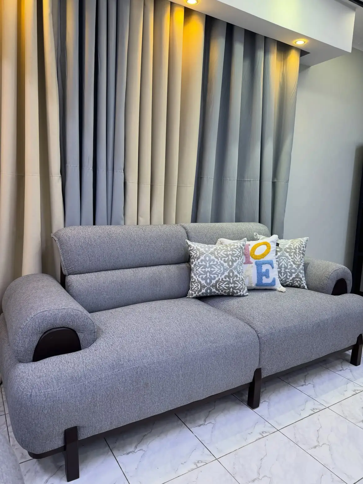 Grey fabric sofa seat with rounded padded arms, cushioned back and raised dark legs Title: Grey 7-Seater Fabric Sofa Set Kenya – Single Seat View