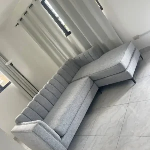 Grey L-shaped sofa with vertical tufted back and extended chaise in a bright living room